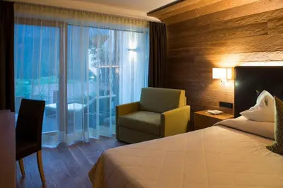 a hotel room with a bed and a chair and a window at Hotel Grien in Ortisei