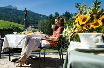 a woman sitting at a table with a cup of coffee at Hotel Chalet Tianes - Alpine Relax in Castelrotto