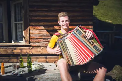 a man holding an accordion in front of a cabin at Obermoserhof in Feldthurns