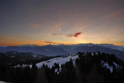 a sunset over a snow covered mountain with a streak of lightning at Hotel-Garni Ehrenfels in Schenna