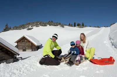 a family sitting in the snow in front of a cabin at Chalet Schmied in Terento