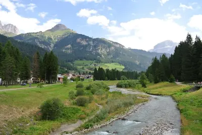 a river in a field with mountains in the background at CasaMau Trilo in Campitello di Fassa