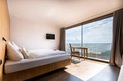 a bedroom with a bed and a desk and a large window at Kronplatz-Resort Hotel Kristall in Valdaora