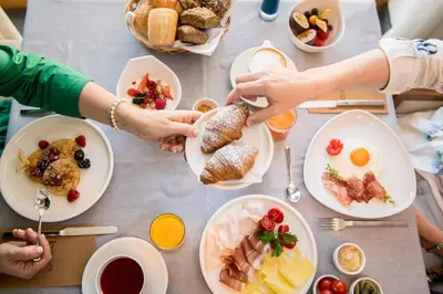a group of people holding hands over a table full of food at Kronplatz-Resort Hotel Kristall in Valdaora