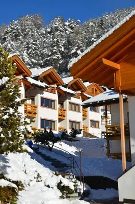 a row of buildings in the snow with snow covered mountains at Residence Des Alpes in Cavalese