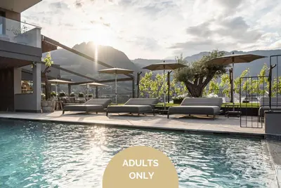a pool with chairs and umbrellas next to a building at Vinea - Apartments in Tirolo