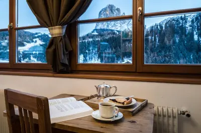 a table with a tea pot and a book and a table with a window at Charme Hotel Uridl in Santa Cristina in Val Gardena
