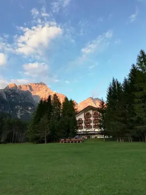 a building in a field with mountains in the background at Hotel il Cardo in San Vito di Cadore