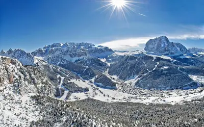 a snow covered mountain range with the sun in the sky at The Oswald Grand Hotel in Selva di Val Gardena