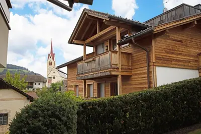 a wooden house with a balcony and a church at Aurturist Valdaora Roulette in Valdaora