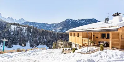 a house on a snow covered slope with mountains in the background at Apartments Milanhof in Ortisei