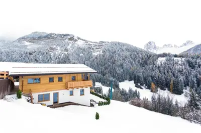 a house on a snow covered hill with a mountain at Apartments Milanhof in Ortisei