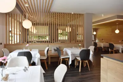 a restaurant with white tables and chairs and windows at X Alp Hotel in Pozza di Fassa