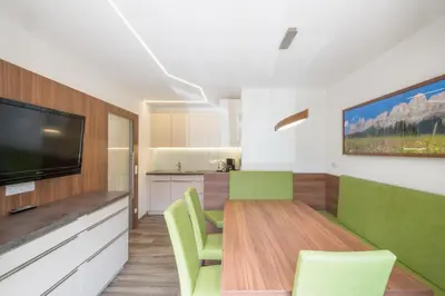 a living room with a dining room table with green chairs at Haus Winkler in Vilpiano
