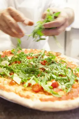 a person is putting toppings on a pizza at Hotel Löwenhof in Bressanone