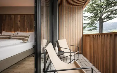 a bedroom with a bed and chairs on a balcony at Hotel Löwenhof in Bressanone