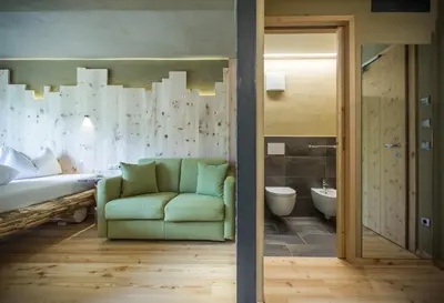 a living room with a green couch and a bathroom at Bike & Ski Hotel Diana Karersee in Nova Levante
