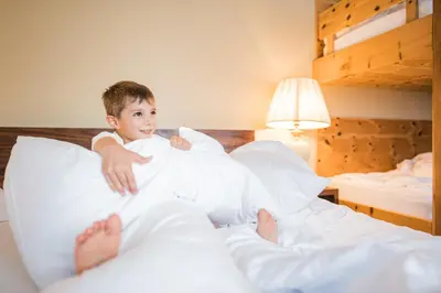 a young boy sitting on a bed with pillows at Hotel Fameli in Valdaora