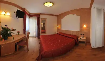 a bedroom with a red bed and a table at Hotel Zirmes in Moena