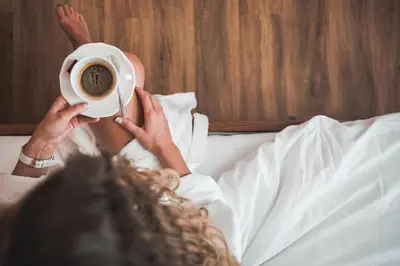 a woman laying in bed holding a cup of coffee at Hotel Am Sonneck in Lagundo
