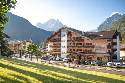a large building with cars parked in a parking lot at Hotel Cristallo in Canazei