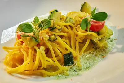 a plate of pasta with tomatoes and basil on it at Hotel Brötz in Rasùn di Sotto