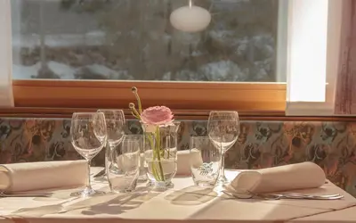 a table with wine glasses and a rose in a vase at Hotel ADLER Carezza in Nova Levante