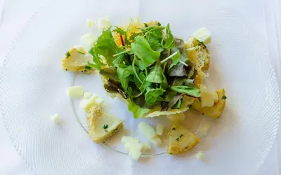 a white plate with a salad and potatoes on it at Hotel ADLER Carezza in Nova Levante