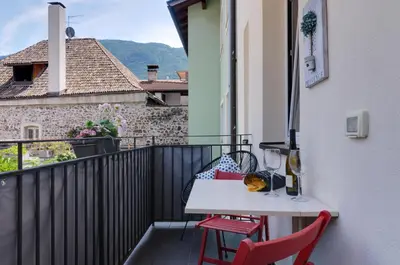 a balcony with a white table and two red chairs at Sonnenuhr Bolzano Apartments in Bolzano
