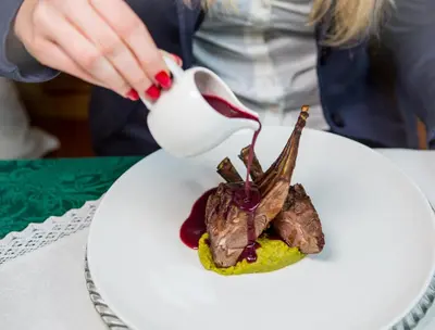 a person pouring sauce onto a plate of food at Historic Hotel Ristorante La Stua in Cavalese