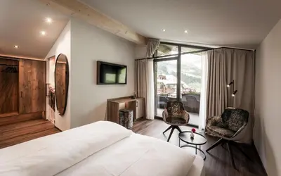 a hotel room with a bed and two chairs at Hotel Belaval in Selva di Val Gardena