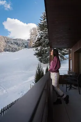 a woman standing on a balcony looking out at the snow at Hotel Belaval in Selva di Val Gardena