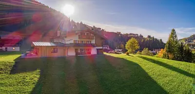 a house in a field with the sun shining on it at Chalet Dumbria Dolomites in Selva di Val Gardena