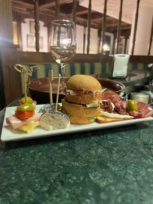a plate with a sandwich and a glass of wine at Hotel Ai Pini in Vigo di Fassa