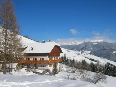 a building on a snow covered slope with mountains at Bigraberhof in Valdaora