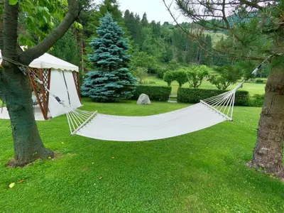 a white hammock hanging from a tree in a yard at Casa Aurora -Altopiano di Pinè in Bedollo