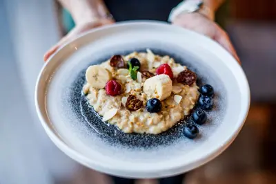 a person holding a bowl of porridge with fruit and nuts at Sporthotel Zoll in Vipiteno