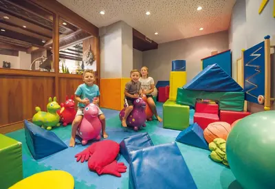 three children sitting on their toys in a play room at Diamant Spa Resort in Santa Cristina in Val Gardena