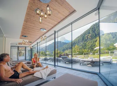 a man and a woman sitting on a couch in a room with windows at Diamant Spa Resort in Santa Cristina in Val Gardena