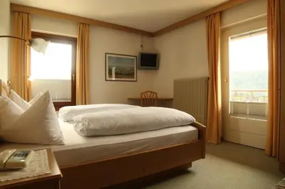 a bedroom with a bed and a desk and a window at gasthof pension rössl in Nova Ponente