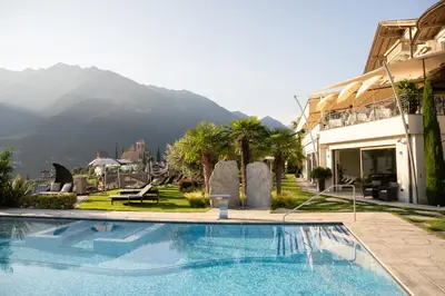 a swimming pool in front of a building with a mountain at Hotel Resmairhof in Schenna