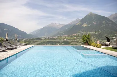 a swimming pool with chairs and mountains in the background at Hotel Resmairhof in Schenna