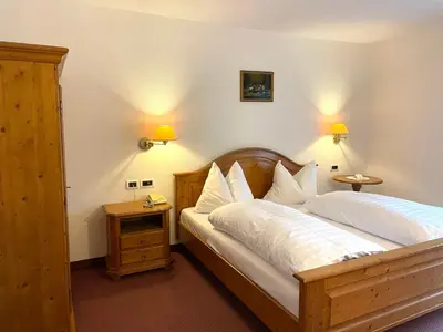 a bedroom with a bed with white sheets and two lamps at Hotel Larch in Campo di Trens