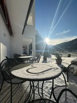 a table and chairs on a patio with the sun shining at Hotel Larch in Campo di Trens