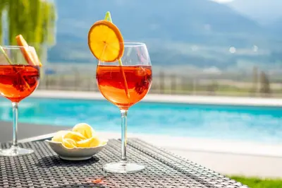 three wine glasses sitting on a table next to a pool at Quellenhof in Termeno