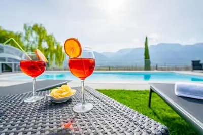 three wine glasses sitting on a table near a pool at Quellenhof in Termeno