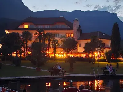 a large building with people sitting on benches near a pond at Seegarten in Caldaro