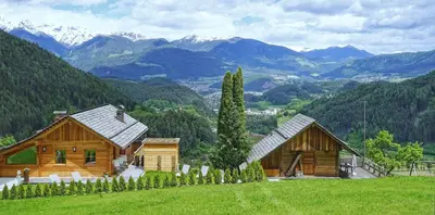 two wooden buildings on a hill with mountains in the background at Chalet Oberguggenberg in San Lorenzo di Sebato