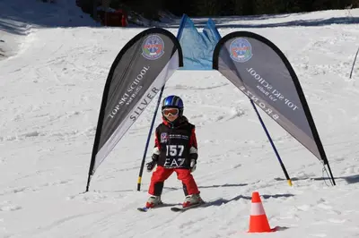 a young child is standing in the snow between two flags at Villa Ortensia in San Vigilio Di Marebbe