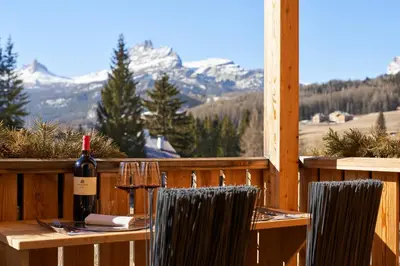 a table with a bottle of wine and two chairs at Dolomiti Lodge Alverà in Cortina dʼAmpezzo